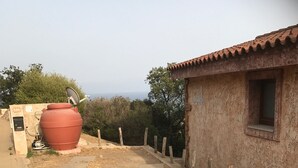 A paved pathway leading to a rustic building with a tiled roof, a large red water tank, and a wooden fence. - Very panoramic 10 minutes walk from the sea (Villaputzu)