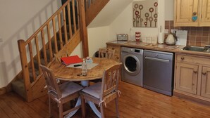Une cuisine avec un plancher en bois, un lave-linge, un évier, des armoires en bois, une table avec des chaises et un escalier.
