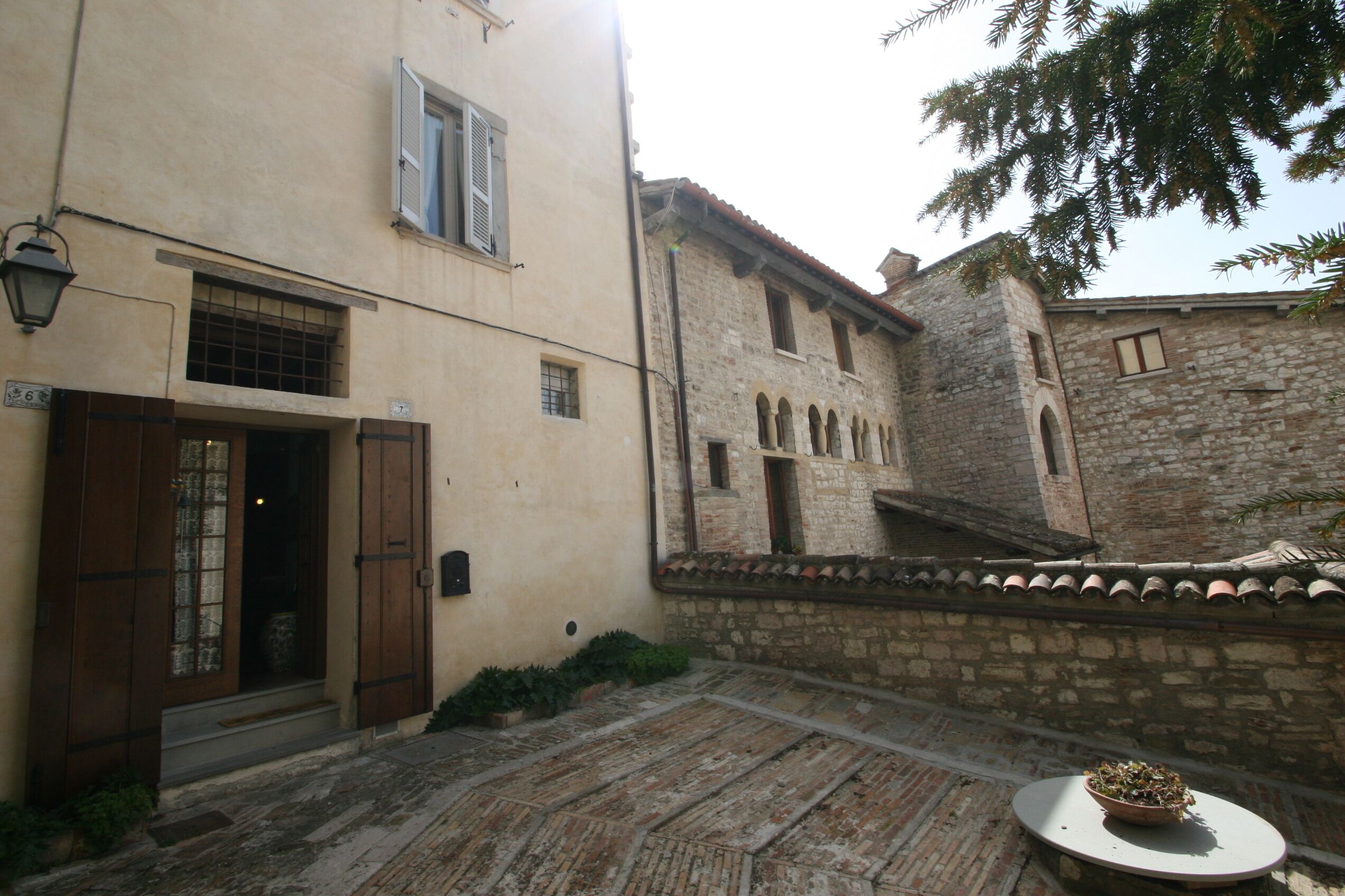 A courtyard with a stone wall, a wooden door, and a small table with a plant.