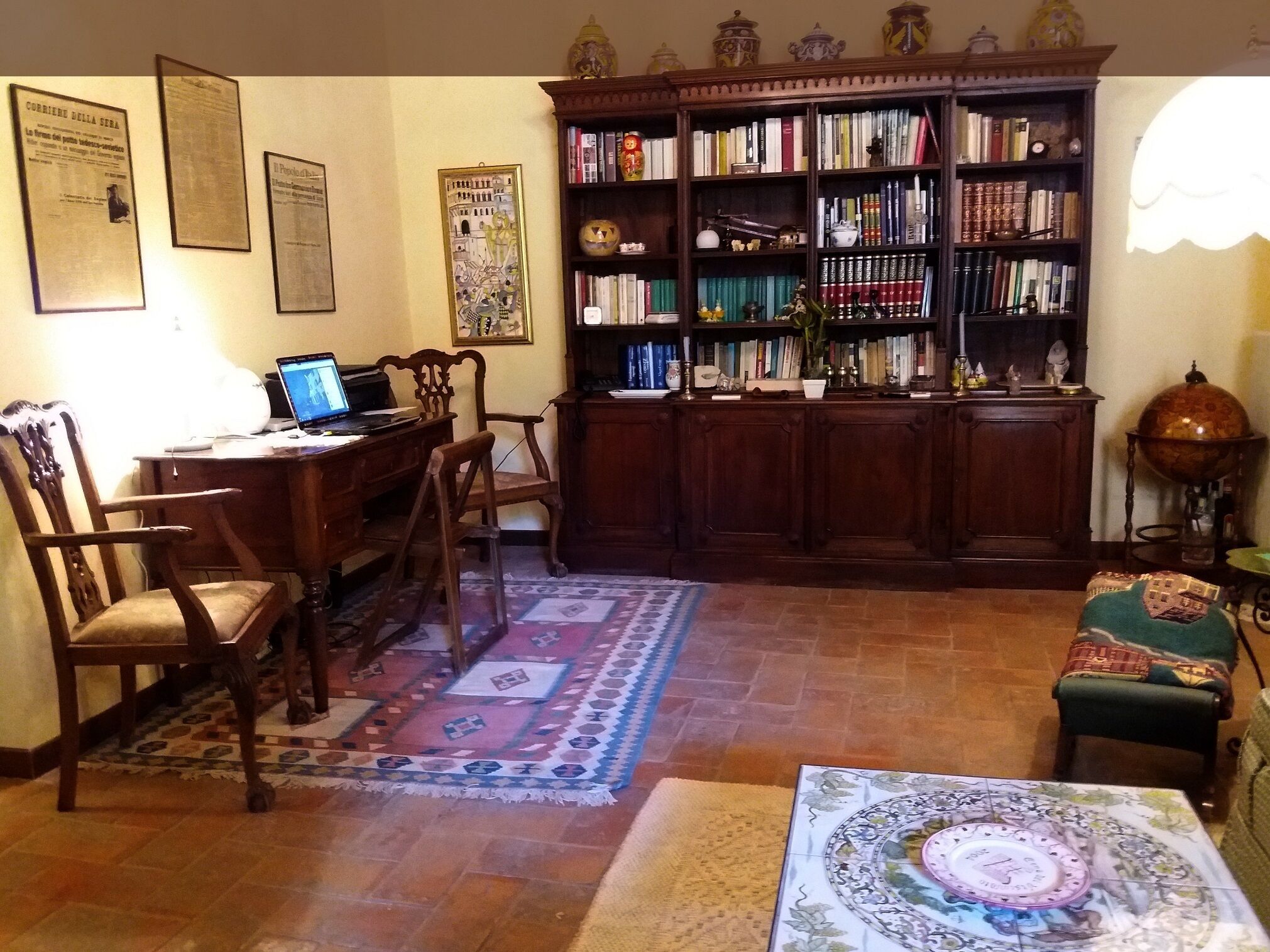 Un salon chaleureux avec un bureau en bois, une bibliothèque remplie de livres, un tapis à motifs et un globe terrestre décoratif.