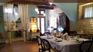 On aperçoit un coin repas avec une table dressée pour quatre personnes, entourée de chaises. Un coin cuisine, avec un four et des placards, est visible sur la gauche.