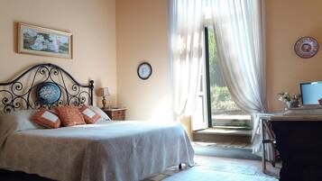 Un dormitorio con cama, mesita de noche, lámpara, reloj y ventana con cortinas.