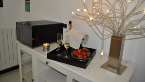 Un dispositivo elettronico nero, due bicchieri di vino bianco, un vassoio con fragole e una lampada decorativa in un vaso su un tavolo bianco.