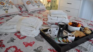 Un letto rifatto con lenzuola a motivi floreali, un vassoio con asciugamani, tazze, biscotti e frutta.