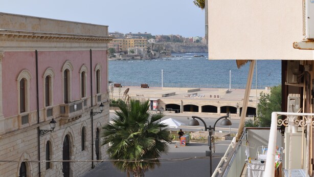 Una strada costiera con un edificio caratterizzato da finestre ad arco e una palma in primo piano.