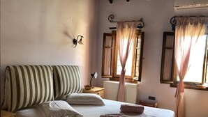 A bedroom with a bed, pillows, a bedside table, a lamp, a window with curtains, and an air conditioning unit. - Villa Maira, Chalkidiki. Holidays as it should be! (Afytos Kassandras Chalkidiki)