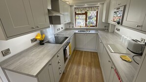 A compact kitchen with grey cabinets, a black induction cooktop, a sink, and a window with a view of the outside. - Self Catering 3 Bedroom Sunset  Haven In Wroxham, Norfolk, Norfolk Broads, Eng (Wroxham)