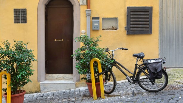 Ein gelbes Gebäude mit einer braunen Tür, einem Blumentopf und einem Fahrrad mit Korb.