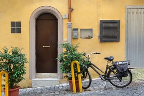 A yellow building with a brown door, a potted plant, and a bicycle with a basket.
