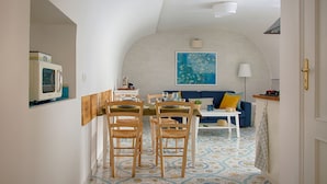 Ein Essbereich mit einem Tisch für vier Personen, Holzsesseln, einer weißen Tischdecke und einem blauen Wandbild darüber.
