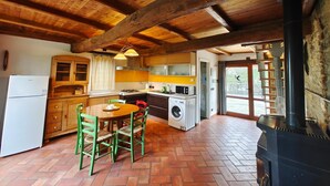 Cozinha rústica com vigas de madeira, mesa de jantar com cadeiras, máquina de lavar roupa e fogão a lenha.