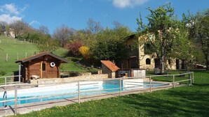 Uma cabana de madeira com uma piscina pequena, cercada por um muro de pedra e uma área gramada.