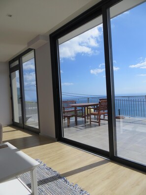 A room with a large sliding glass door leading to an outdoor patio with a table and chairs. - Apartment Goncalves, dazzling view over sea and mountains (Arco da Calheta)