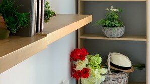 Rincón de una habitación con estanterías de madera que exhiben libros, plantas y un retrato enmarcado.