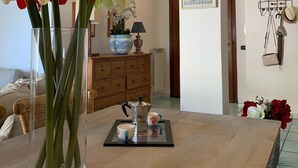 Una habitación con una mesa de madera, un jarrón con flores, una cafetera y un cuadro en la pared.