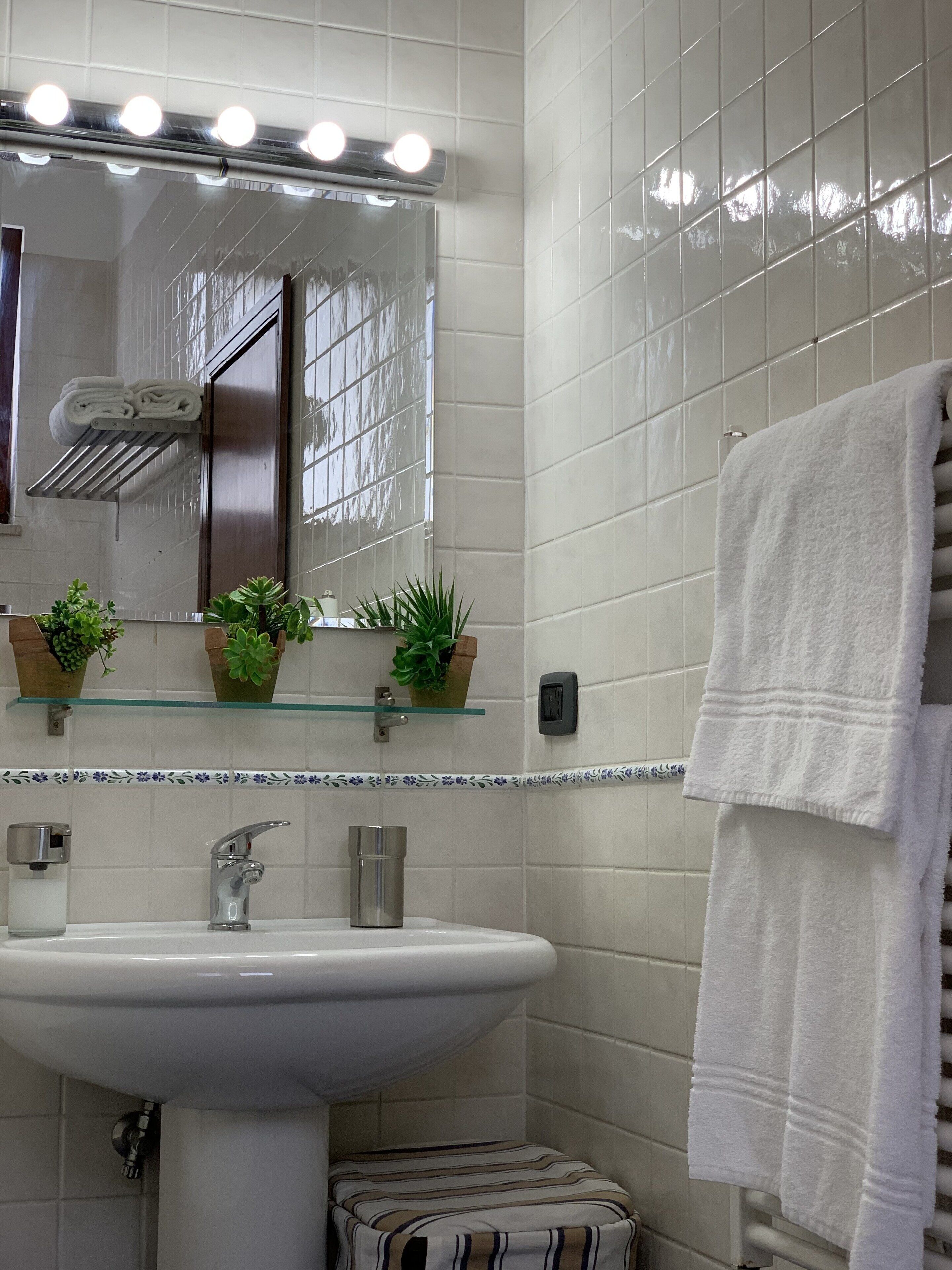 A bathroom with a white sink, a mirror with lights, and a towel rack.