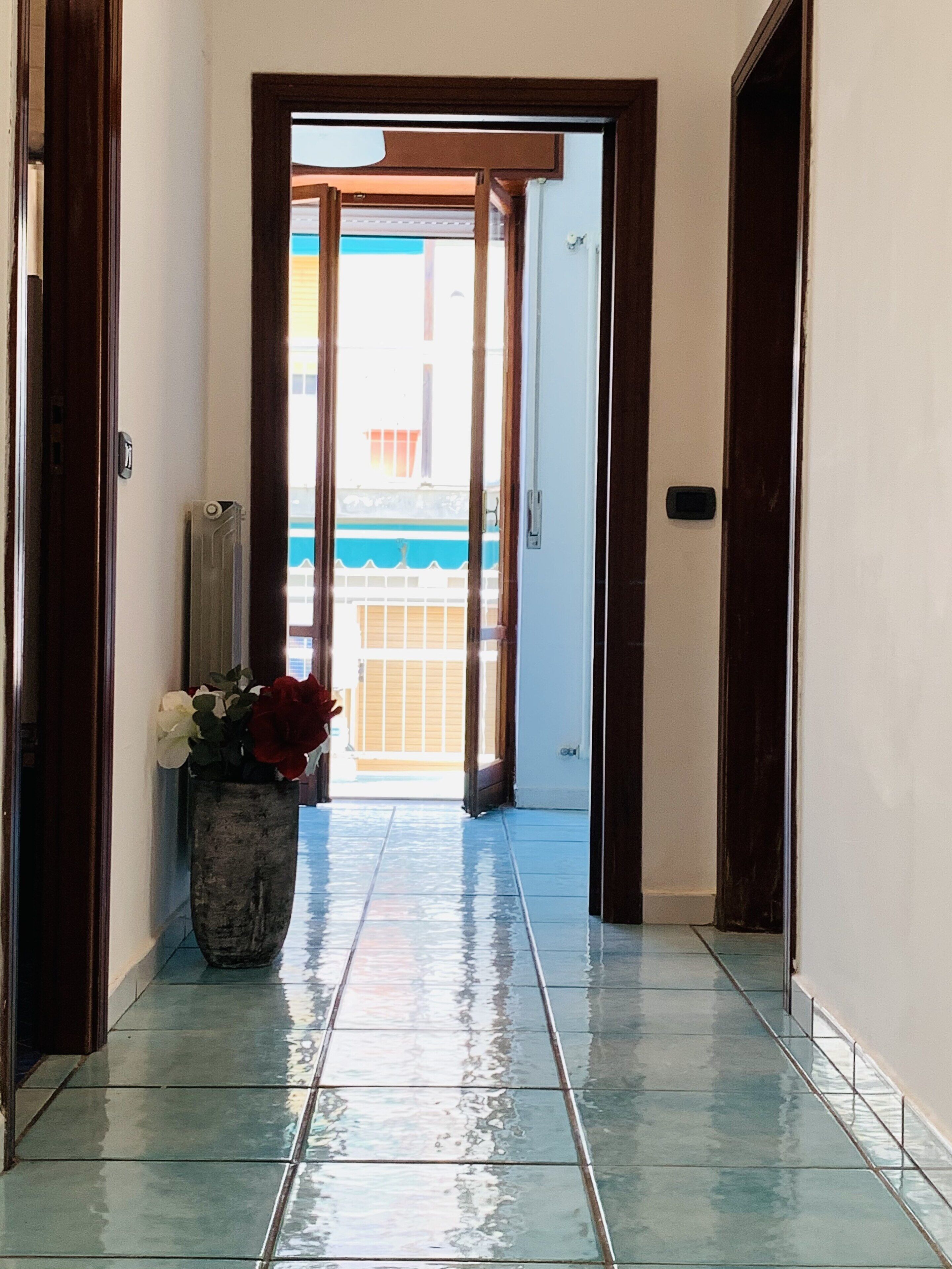 A hallway with a tiled floor leading to a door with a view of a balcony.