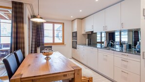 A modern kitchen with white cabinets, a wooden dining table, and a large window. - Panoramapark Soleil Camelia Apt. Akroyd (Wengen)