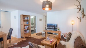 A cozy living room with a sofa, a coffee table, a bookshelf, a television, and a decorative antler. - Panoramapark Soleil Camelia Apt. Akroyd (Wengen)