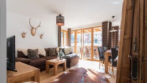 A cozy living room with a wooden sofa, a coffee table, and a leather rug. There are antlers on the wall and a fireplace. - Panoramapark Soleil Camelia Apt. Akroyd (Wengen)