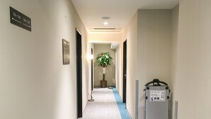 Un couloir d’hôtel avec des panneaux de signalisation, une plante en pot et un coffret électrique.