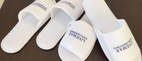 Four white slippers with "LIVEMAX" printed on them, placed on a dark wooden surface.