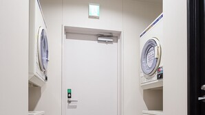 Un couloir étroit, avec une porte au fond, et de part et d’autre, deux machines à laver.