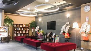 Un hall d’entrée moderne avec des sièges rouges, un comptoir d’accueil, une horloge et des plantes décoratives.