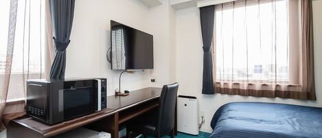 Una habitación de hotel con cama, escritorio, computadora, televisor y microondas.