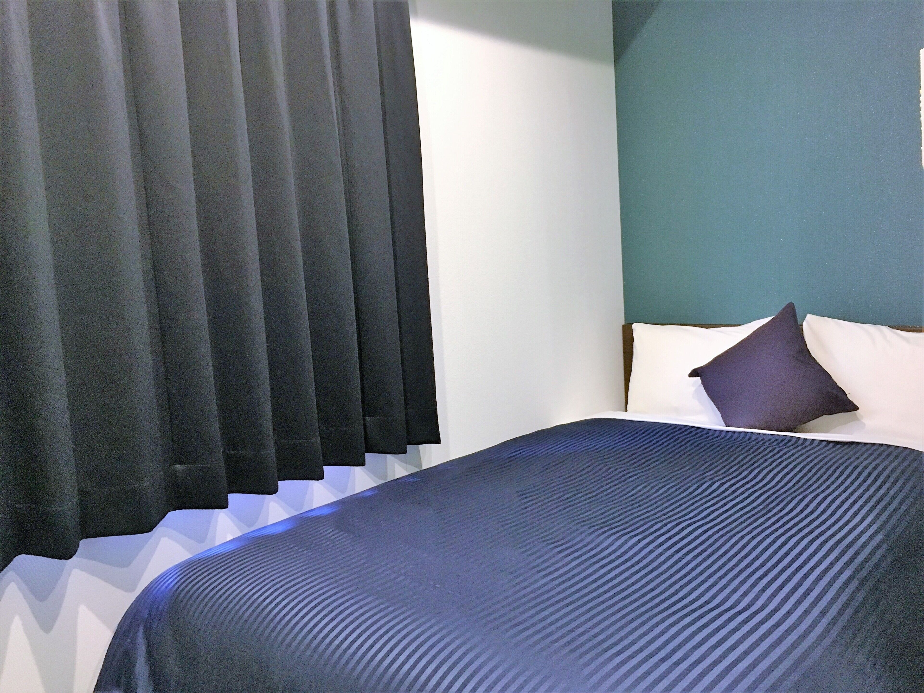A bed with a blue bedspread, two pillows, and a headboard against a teal wall.