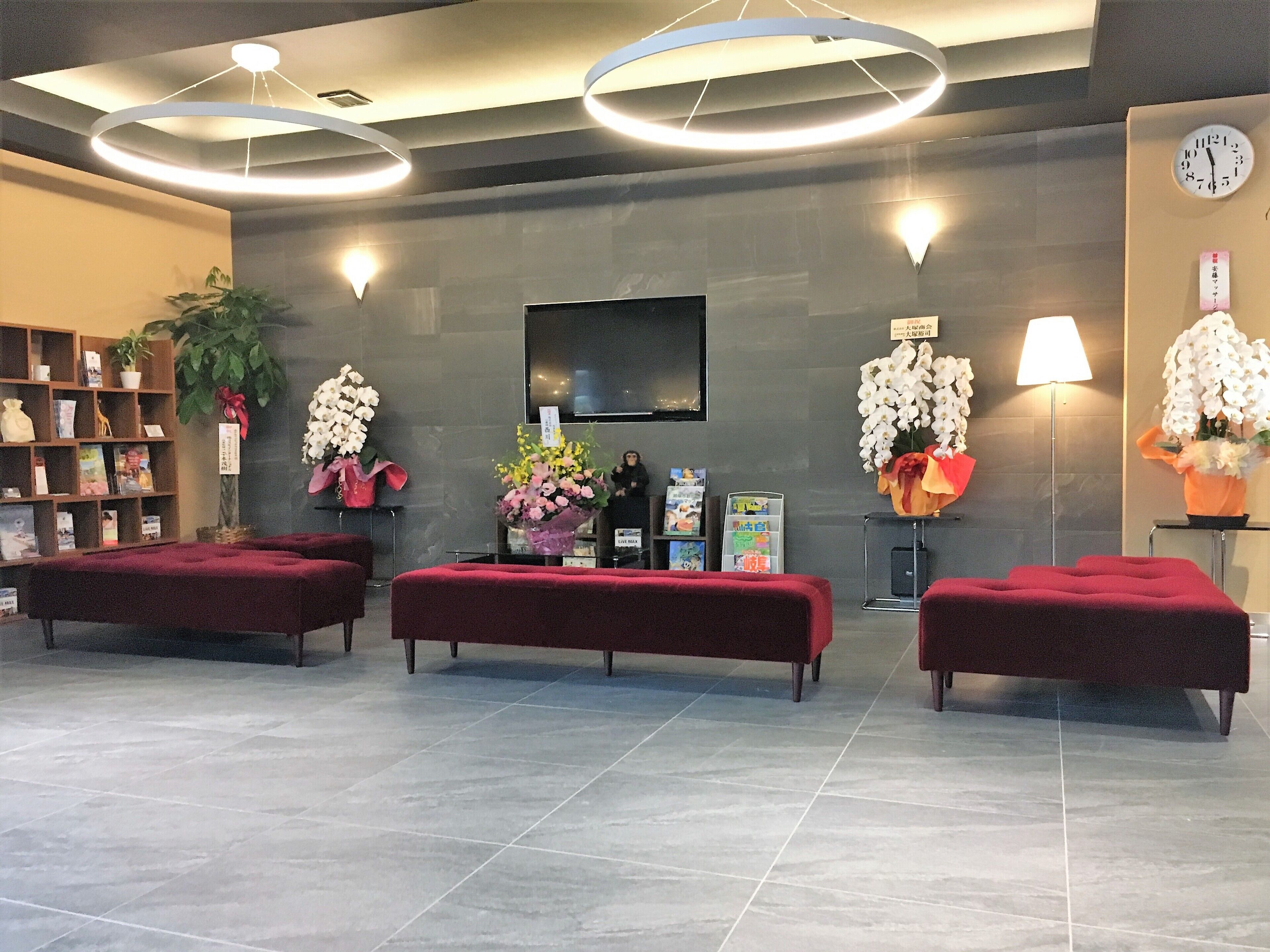 A lobby with a reception desk, two red sofas, a bookshelf, a clock, and a TV screen.