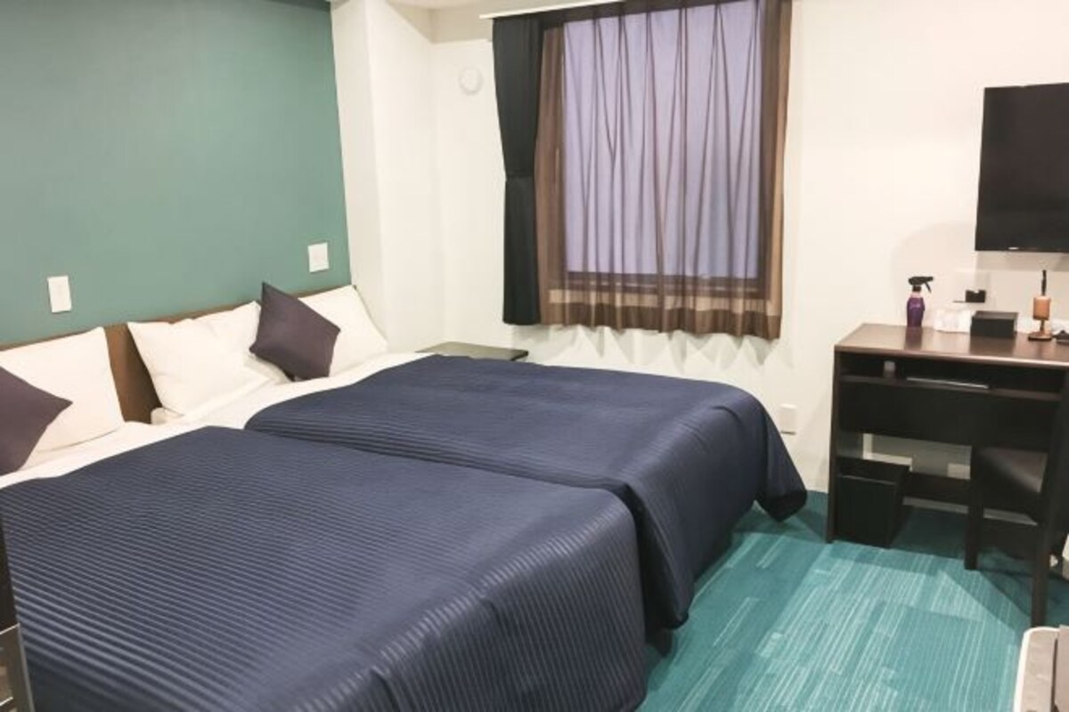 Una camera d'albergo con due letti, una scrivania, un televisore e una finestra con tende.