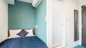 Une chambre avec un lit, un climatiseur fixé au mur, une porte et une petite fenêtre.