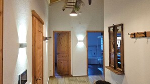 Ein schmaler Flur mit Holzböden und schräg verlaufender Decke. Zwei Holztüren, eine Bank und ein Spiegel befinden sich an der rechten Wand.