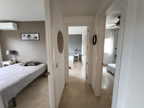 Une chambre d’hôtel comprenant un lit, une table de chevet, une lampe et donnant sur la chambre adjacente.