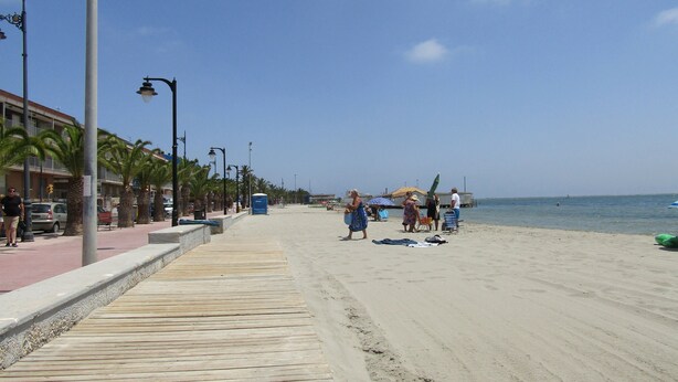 A beach with a wooden boardwalk, palm trees, and a clear sky.