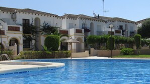 A swimming pool with a tiled edge, surrounded by a building with a tiled roof and white walls.