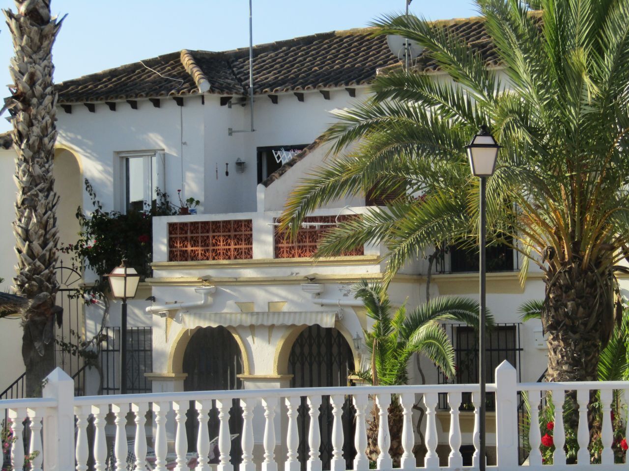 Un bâtiment blanc avec un toit recouvert de tuiles, des fenêtres en arc de cercle et une clôture blanche ornée de balustres.