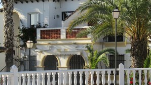 A white building with a tiled roof, arched windows, and a white fence with balusters.