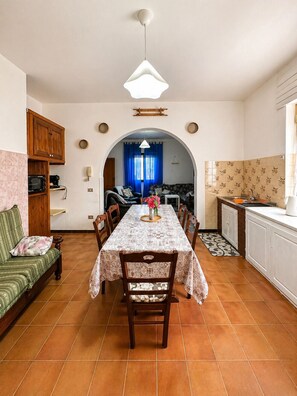 A dining area with a table set for four, a kitchen with a sink and cabinets, and a living area with a sofa and a television. - Giba holiday home near the sea (Giba)