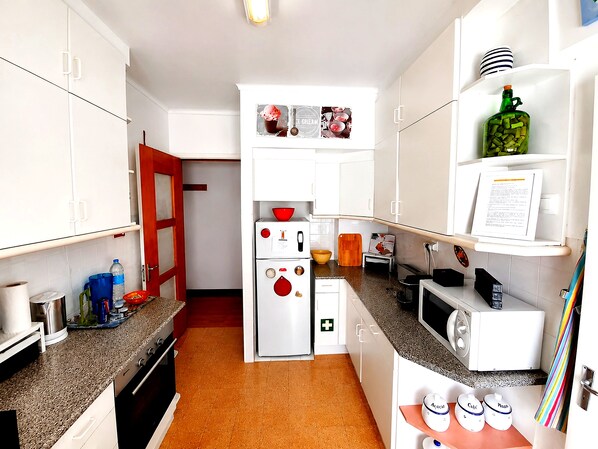 A compact kitchen with white cabinets, a refrigerator, a microwave, and a small countertop area.