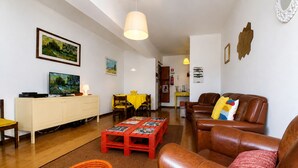 Un salon avec un canapé en cuir marron, une table basse rouge, un téléviseur et un coin repas avec des chaises jaunes.