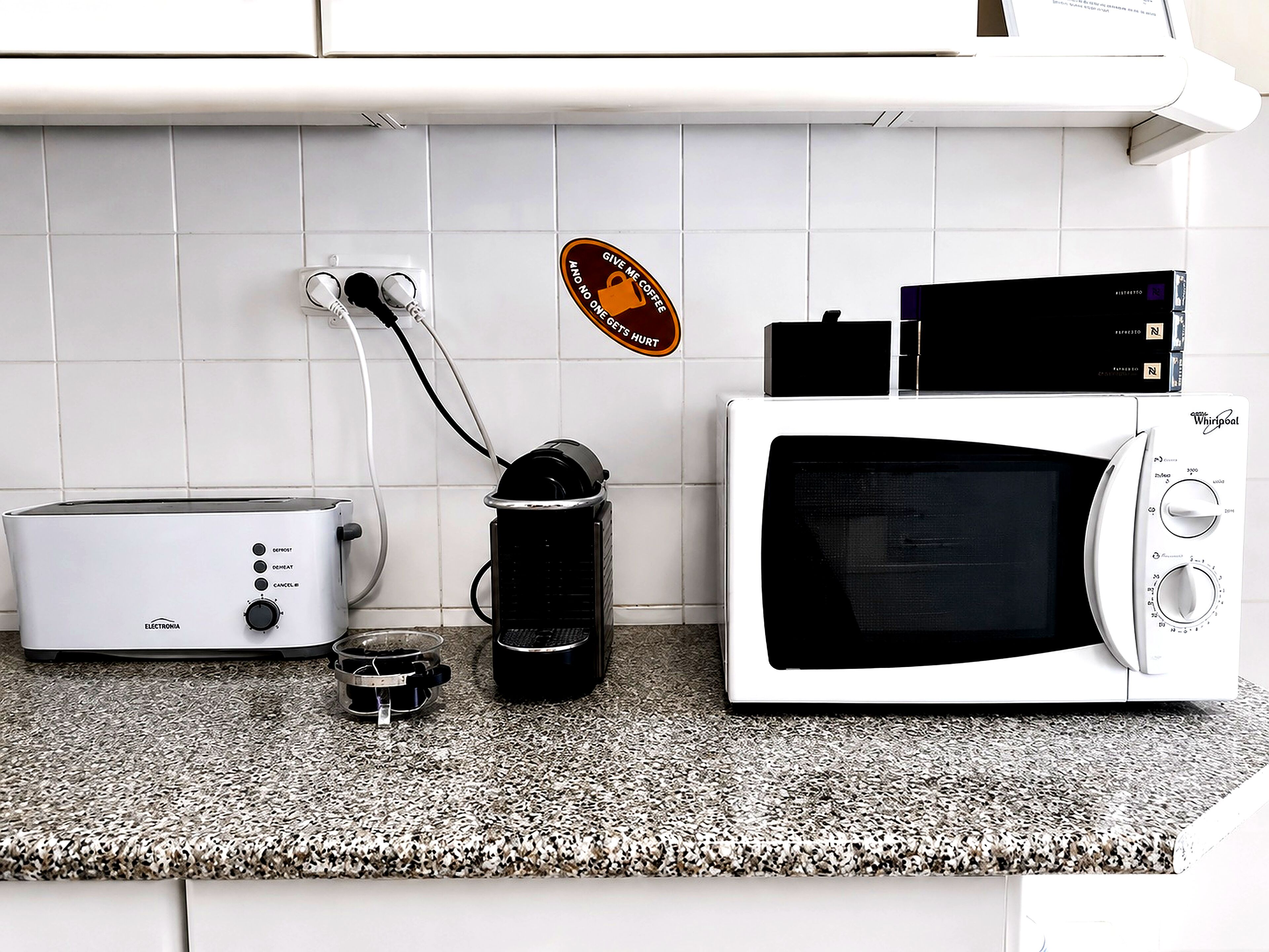 A kitchen with a toaster, a coffee maker, and a microwave on a granite countertop.