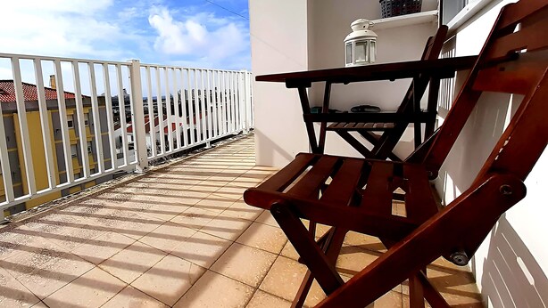 Een balkon met een houten stoel, een tafeltje en een witte lantaarn.