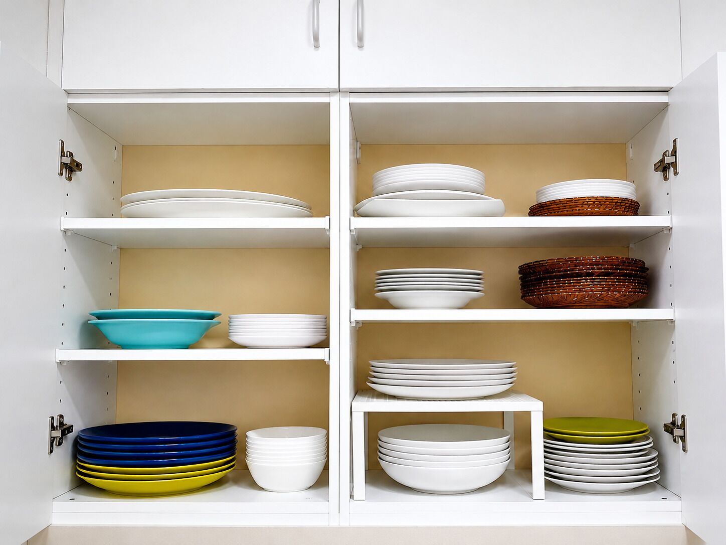A white cabinet with multiple shelves containing stacks of white plates, bowls, and a few colorful bowls.