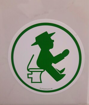 A circular sign with a green silhouette of a person sitting on a stool, holding a book.