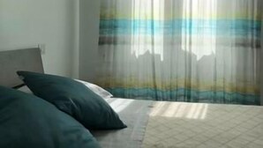 Une chambre à coucher avec un lit, des oreillers et une fenêtre ornée de rideaux légers.
