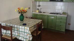 A kitchen with green cabinets, a tiled backsplash, a stove, and a dining table with a checkered tablecloth.