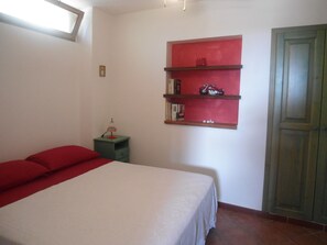 Quarto com uma cama, uma mesa de cabeceira, uma estante vermelha com livros e uma miniatura de motocicleta, e uma porta verde.