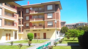 A multi-story residential building with balconies, a courtyard with green benches, and a clear blue sky. - Residential tourist use with WiFi (Villarcayo)